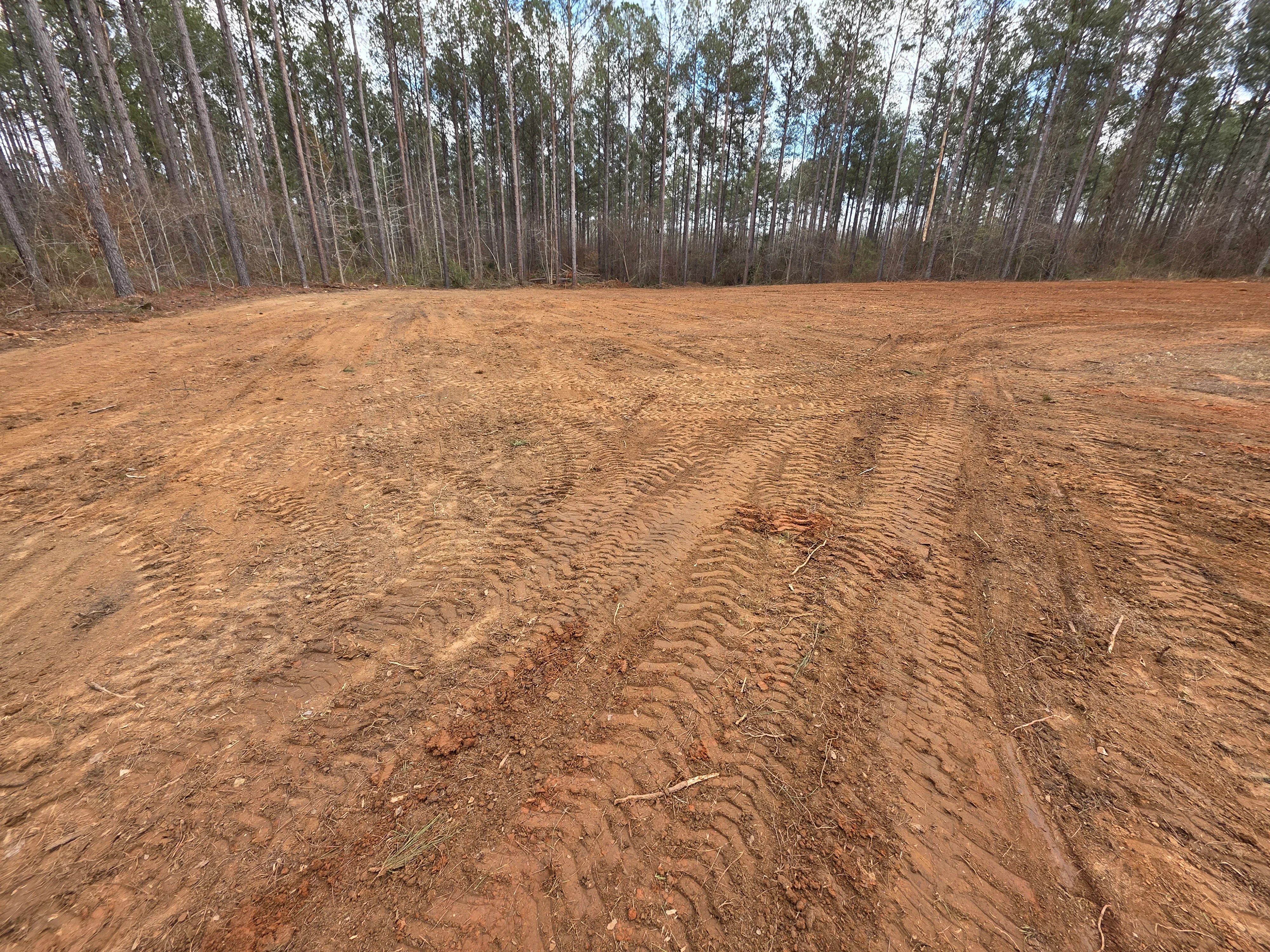 Cleared and graded dirt lot with tree line in background, ready for development