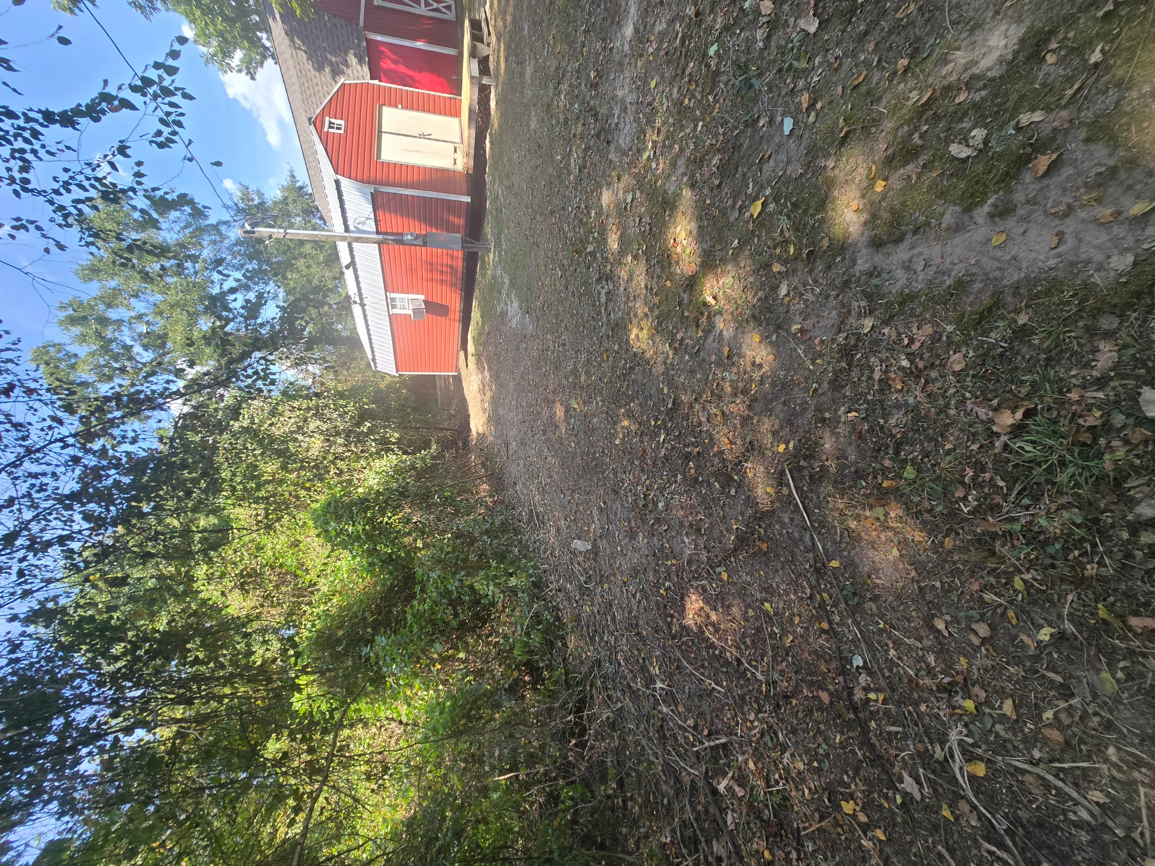 Cleared driveway with removed vegetation and debris, red barn structure visible in background