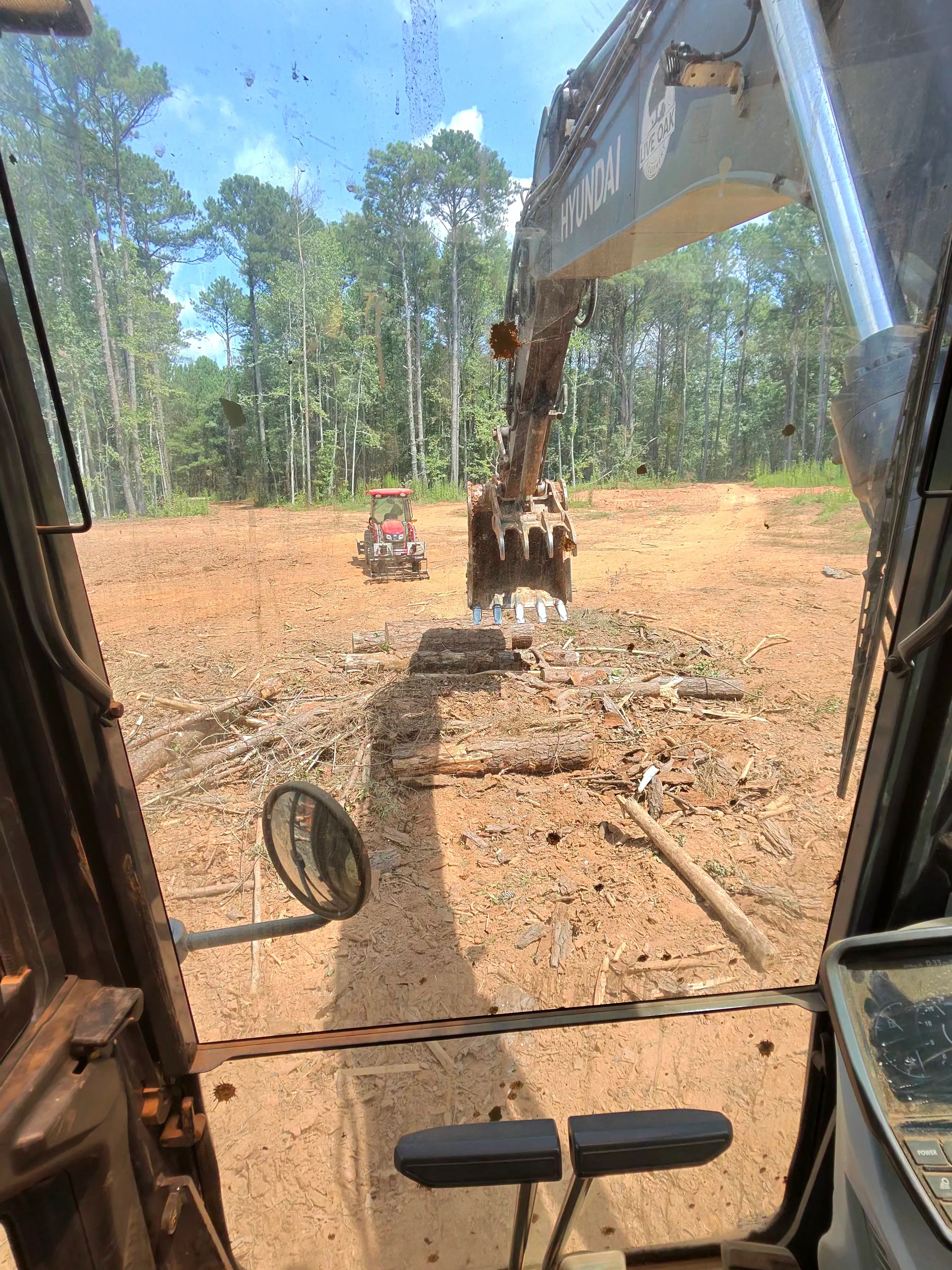 Excavator with grapple bucket removing felled tree on cleared dirt lot