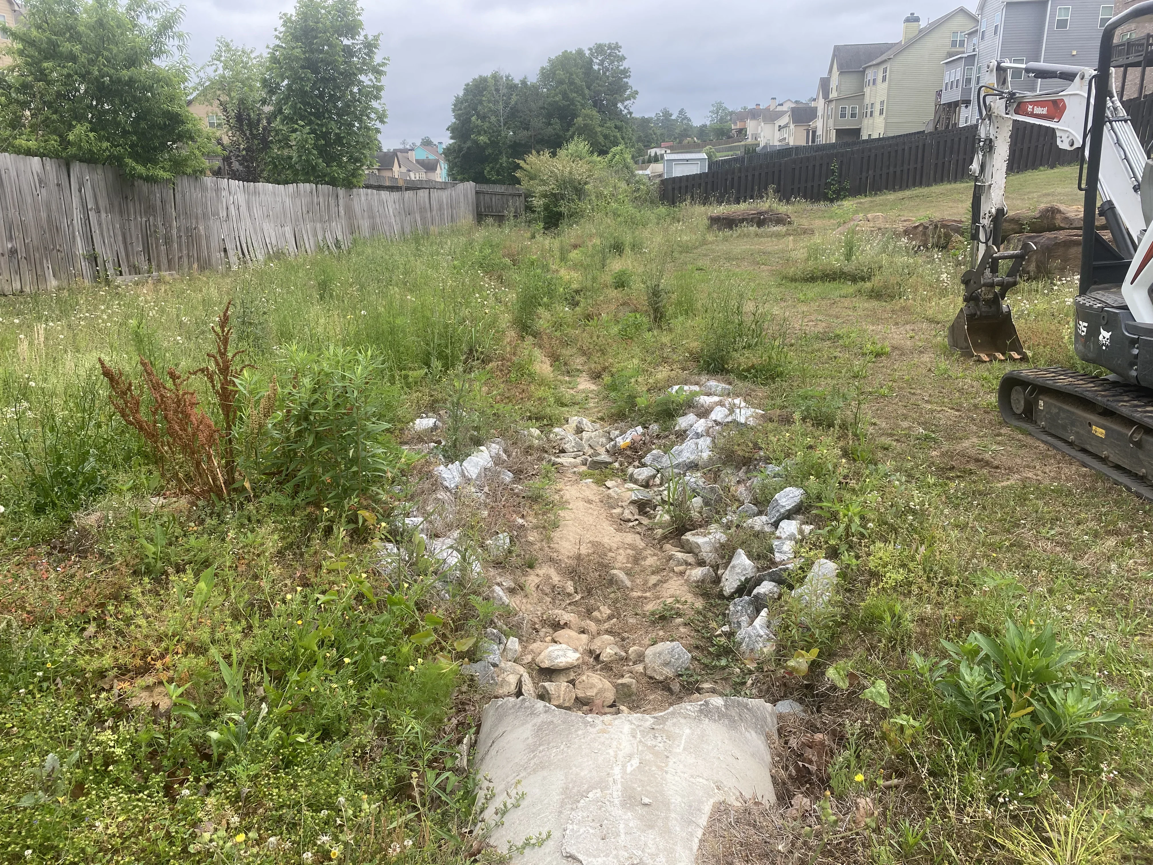 Cleared lot with rock and concrete debris removal, excavator on site