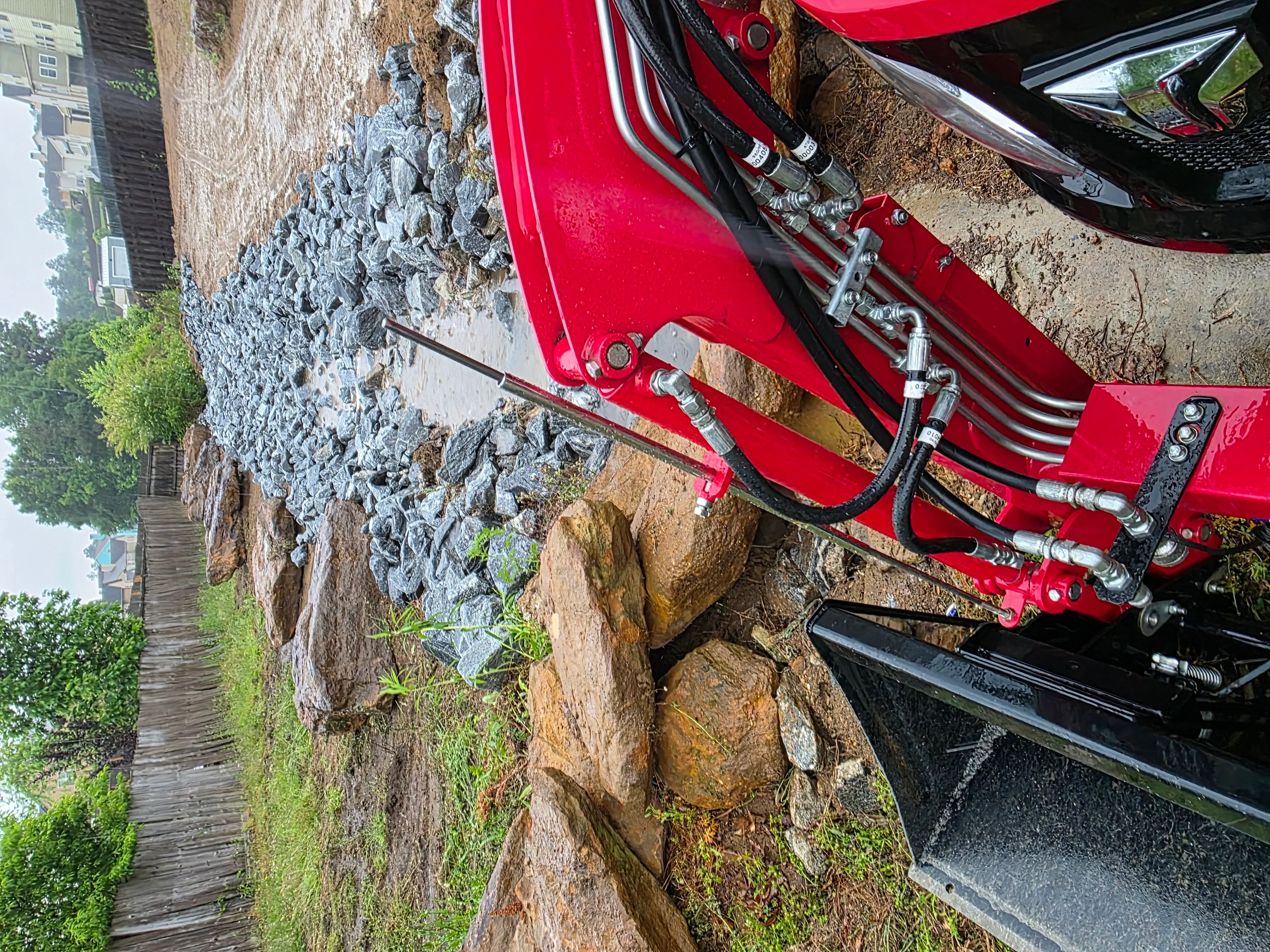Red hydraulic demolition equipment breaking up concrete foundation with metal reinforcement visible