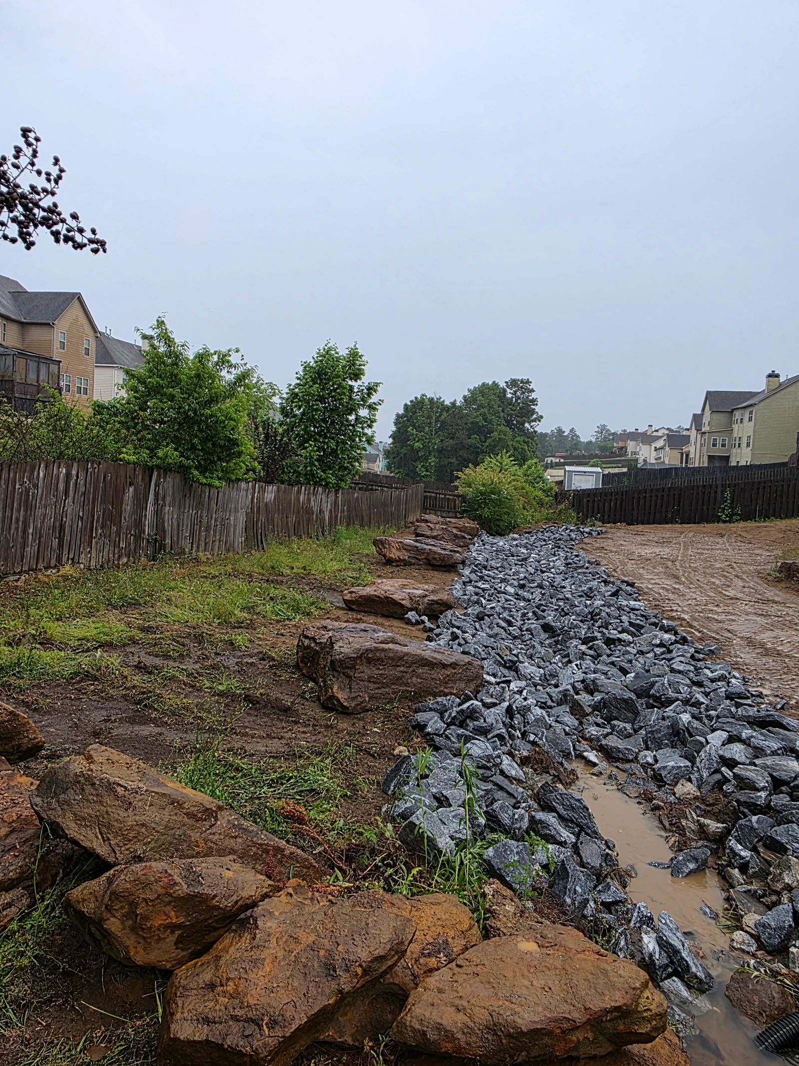 Boulder and crushed stone drainage rock installation along erosion control line with cleared soil base