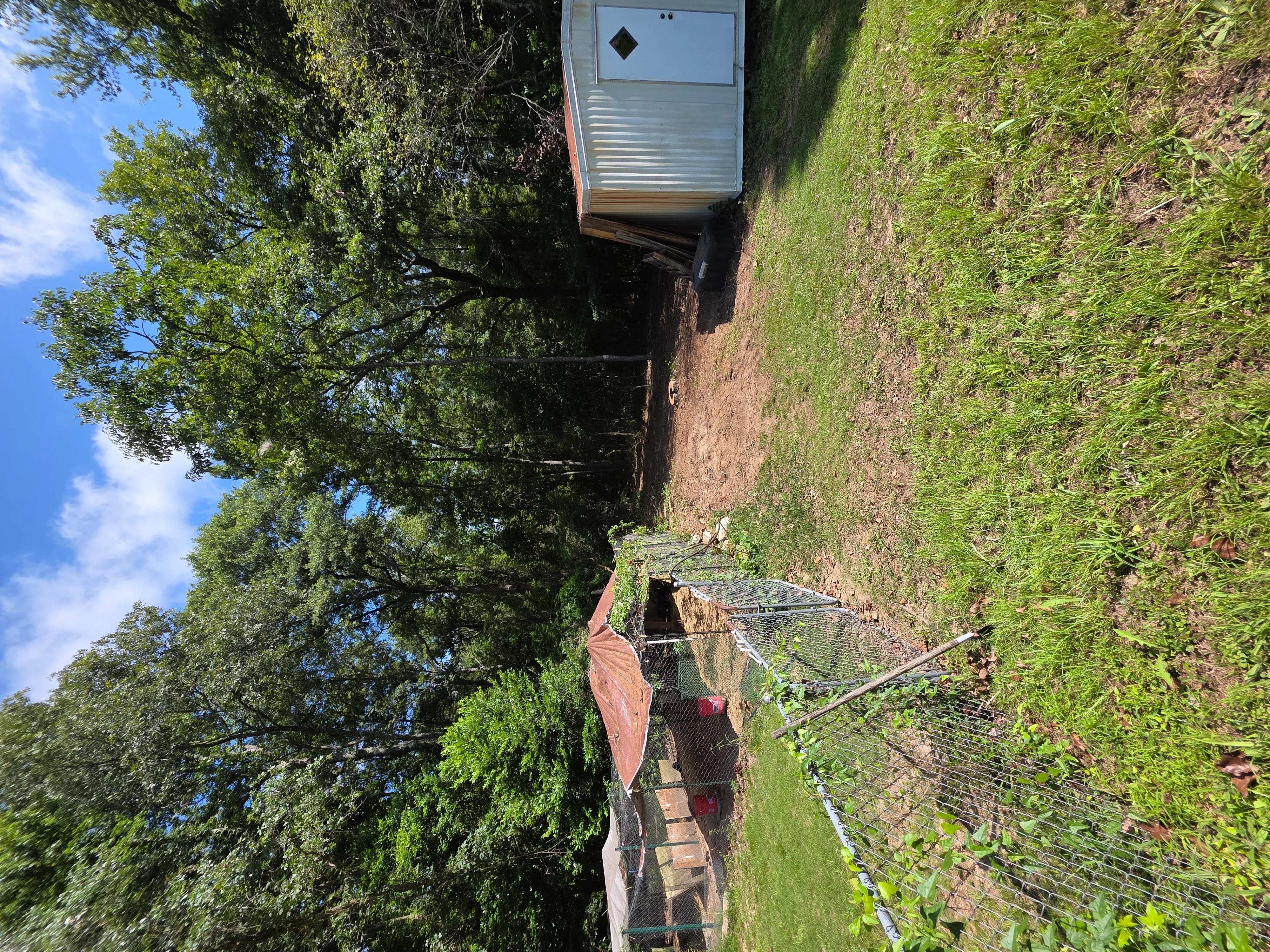 Demolished residential building foundation with brick chimney, metal roof debris, and cleared lot surrounded by trees