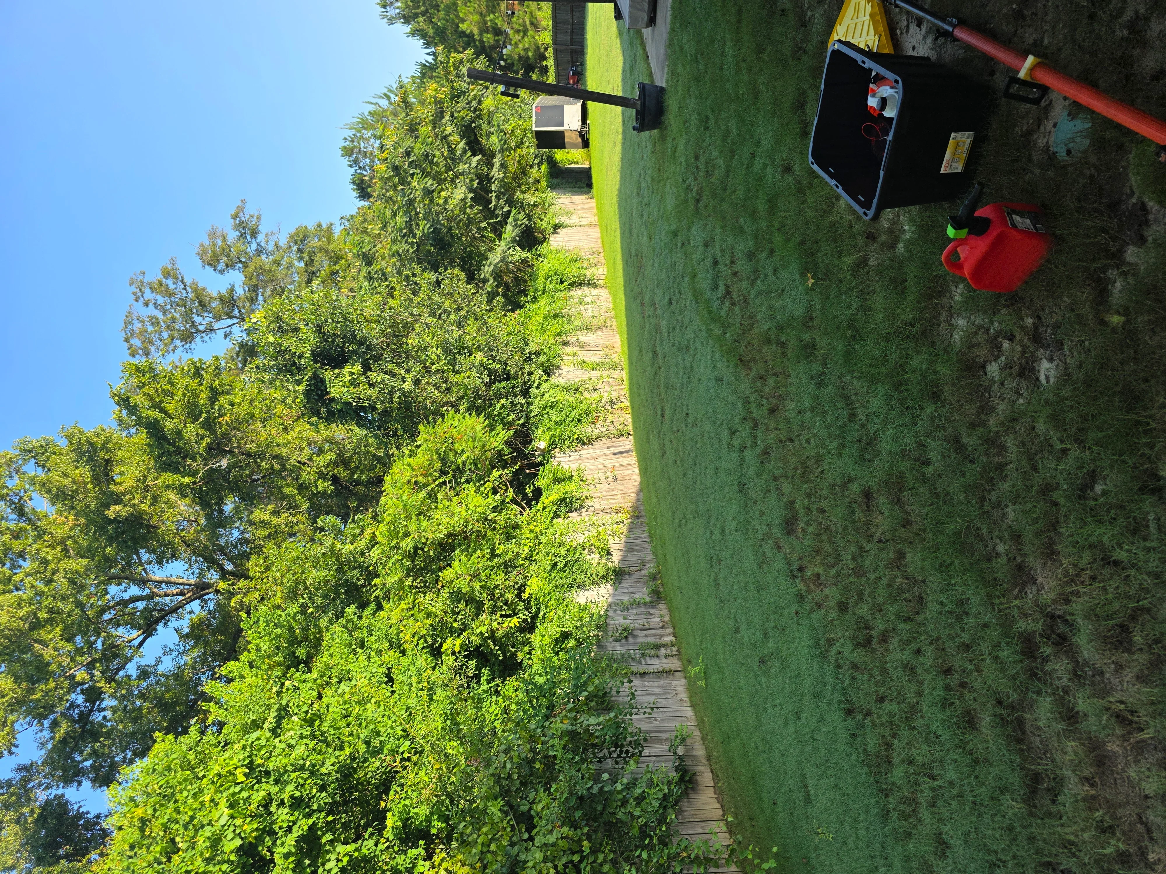 Cleared residential yard with green lawn, wooden walkway, and debris removal equipment staged on property