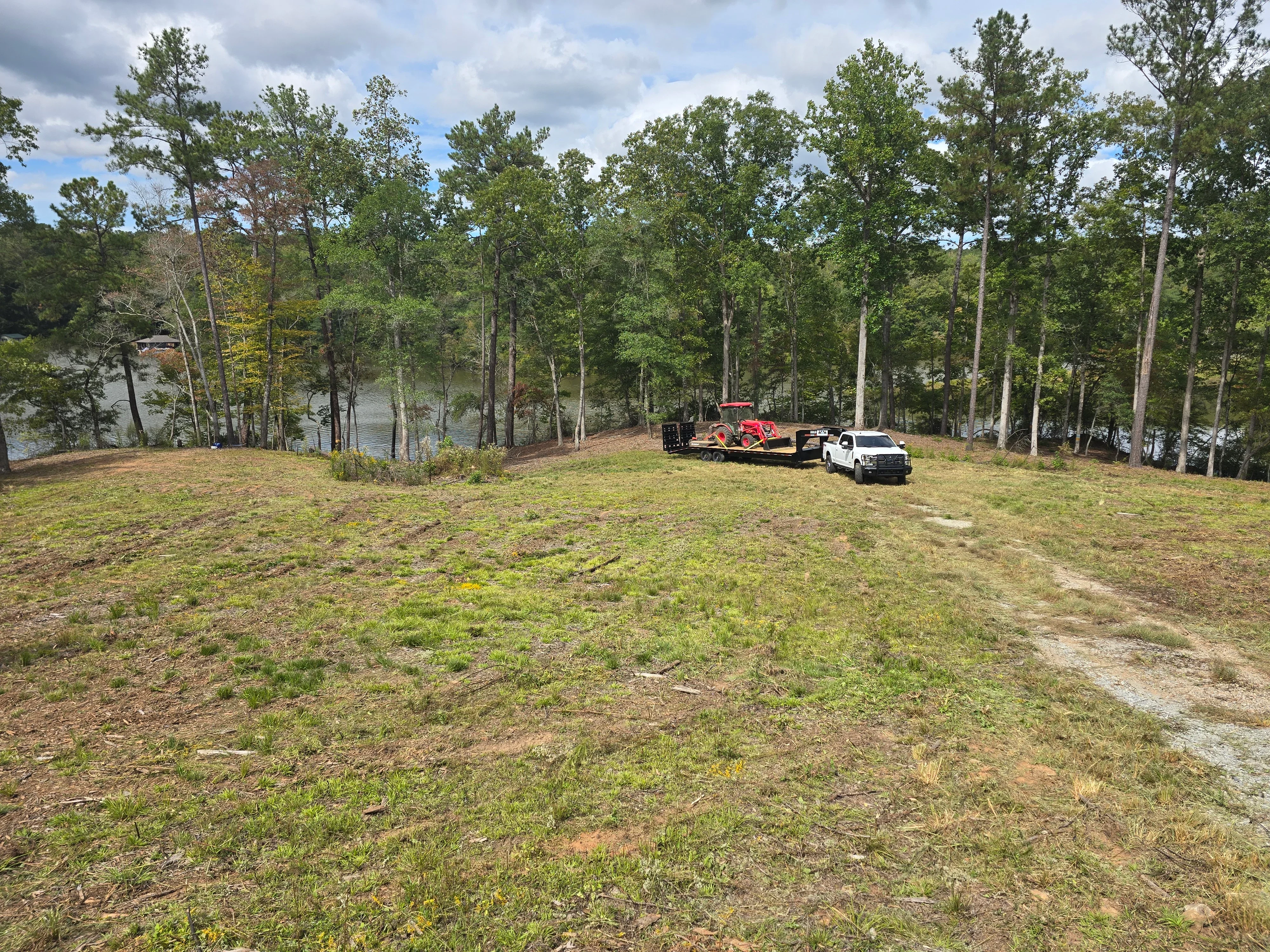 Cleared waterfront lot with timber trees, heavy equipment and dump trailer on bare ground