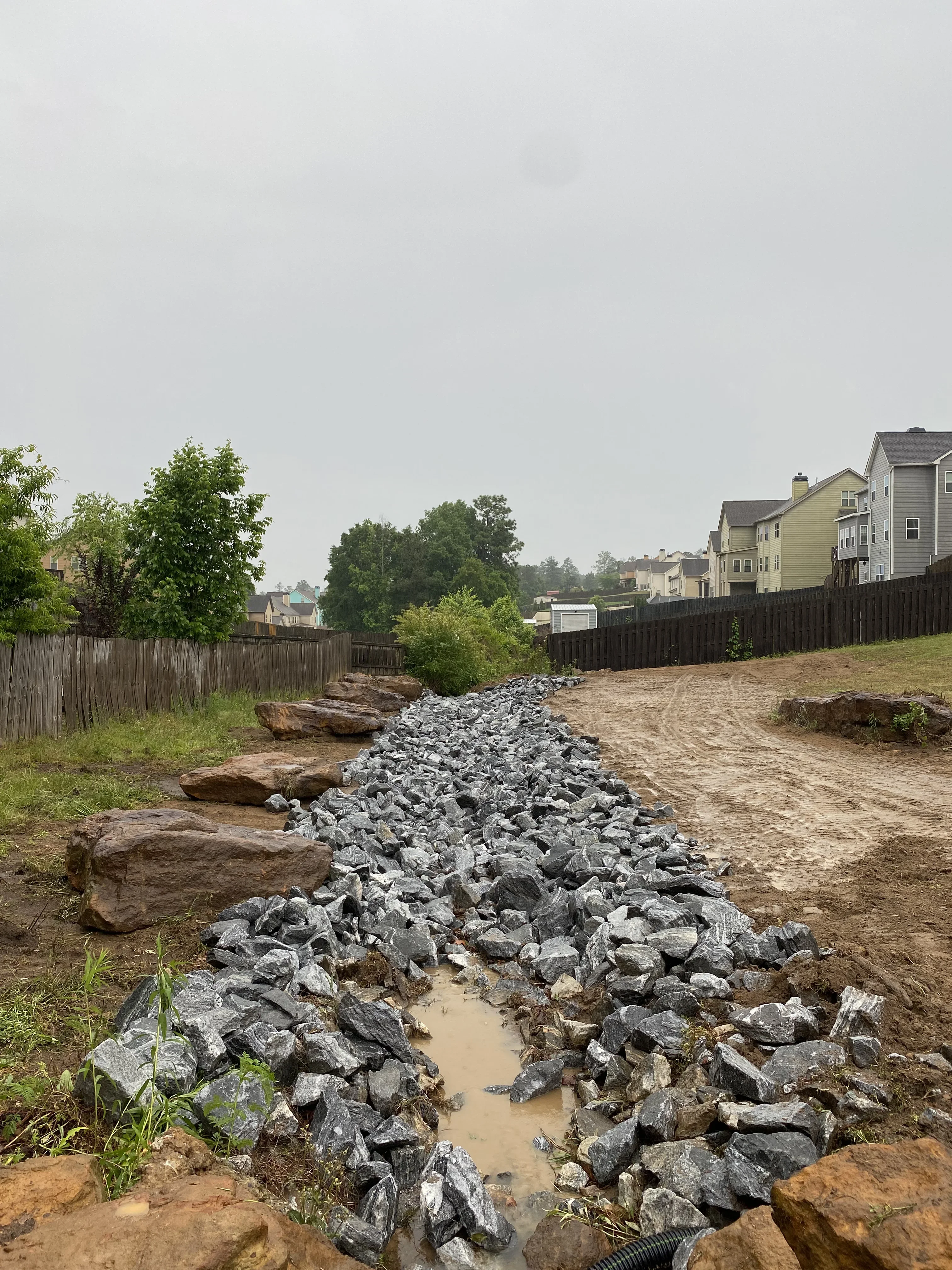 Riprap stone erosion control barrier with granite boulders along cleared residential site
